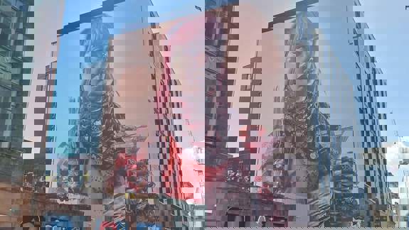 A striking mural of a woman with pink hair, holding a lit candle and a martini glass. The mural covers the side of a large building, The Social Hub,  with smaller street art visible below.