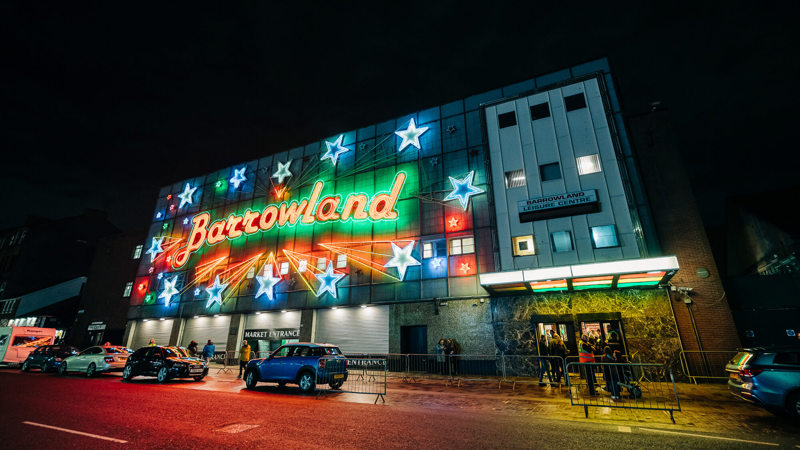 The Barrowland Ballroom at night, brightly lit with neon stars and its name, with cars and people outside.