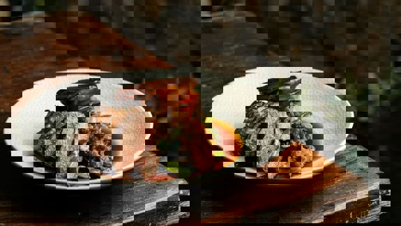 A close-up of a plated meal with sliced meat, a large potato, and vegetables in sauce.