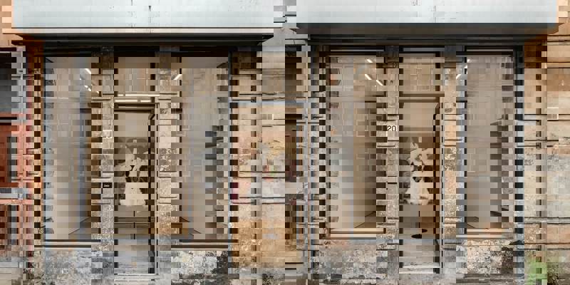 Storefront gallery with three windows and an open door. An art piece with white fuzzy figures is visible inside.