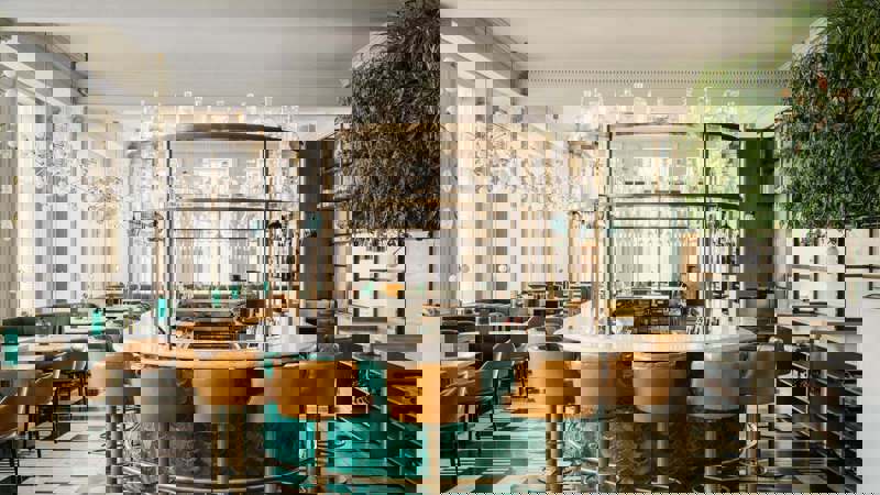 A refined bar with contemporary Scottish decor, navy-blue banquettes, soft overhead lighting, marble tabletops, and neatly arranged bottles behind the counter.