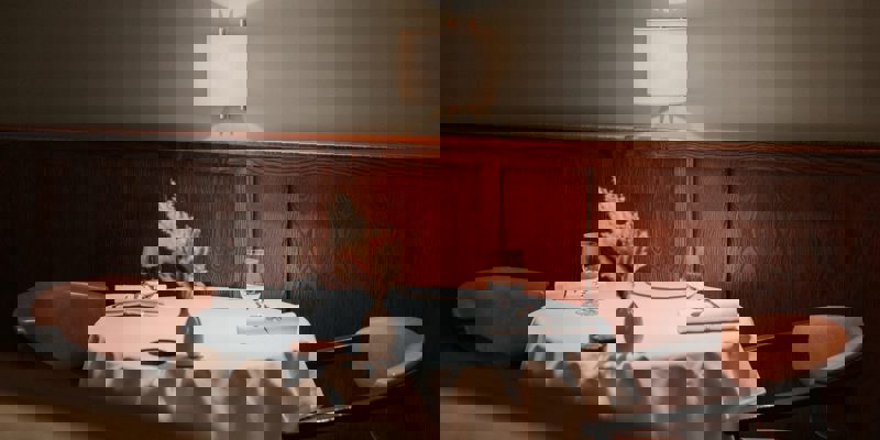 A round, white-clothed table for two with empty wine glasses, napkins, and a small flower arrangement.