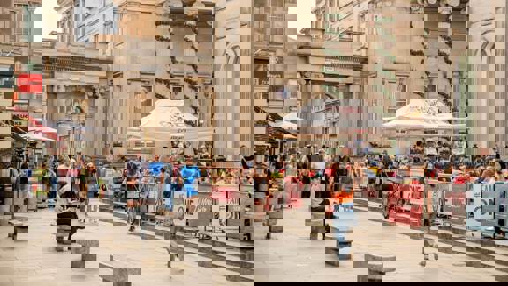 Royal Exchange Square in Glasgow, bustling with people enjoying outdoor dining and walking amongst the grand classical buildings, with a Starbucks visible.