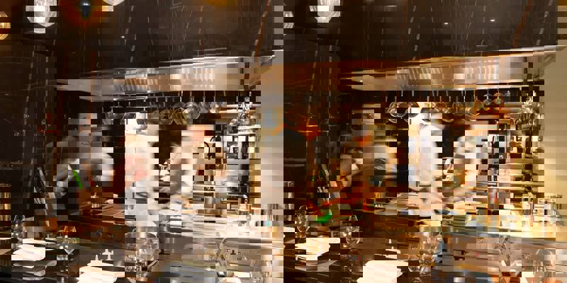 Chefs work in a bustling, modern kitchen with a black marble countertop and hanging lights.