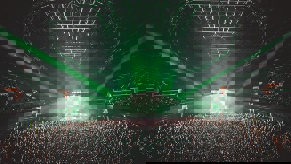 An interior shot of the OVO Hydro arena, filled with a large crowd and lit by green stage lights.