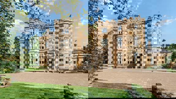 Grand exterior of Crossbasket Castle surrounded by manicured lawns and gardens, showcasing its historic stone architecture and turreted façade on a bright day.