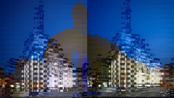 The Gallery of Modern Art (GOMA) at night, with its classical facade and columns dramatically lit against a dark blue sky.