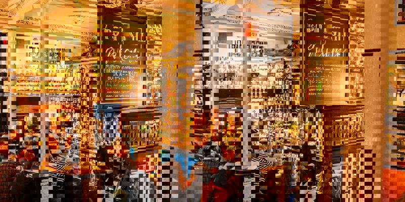 A crowded bar scene at The Pot Still pub, filled with rows of whisky bottles.