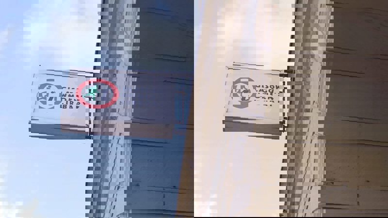 A white sign with a red circle logo and "Glasgow Women's Library" hangs from a stone building.