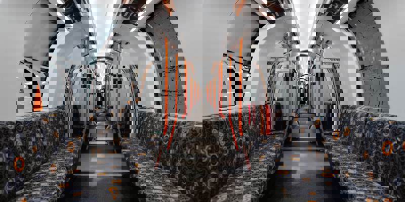 The sleek, modern interior of a Glasgow Subway train, featuring a white ceiling with orange lights and patterned grey seats.