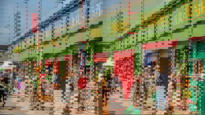 People browse goods at outdoor stalls with green and red storefronts at The Barras Market.