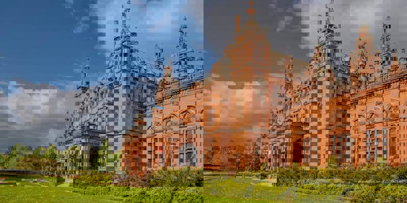 A large, red brick building with a grand entrance, surrounded by a green lawn.