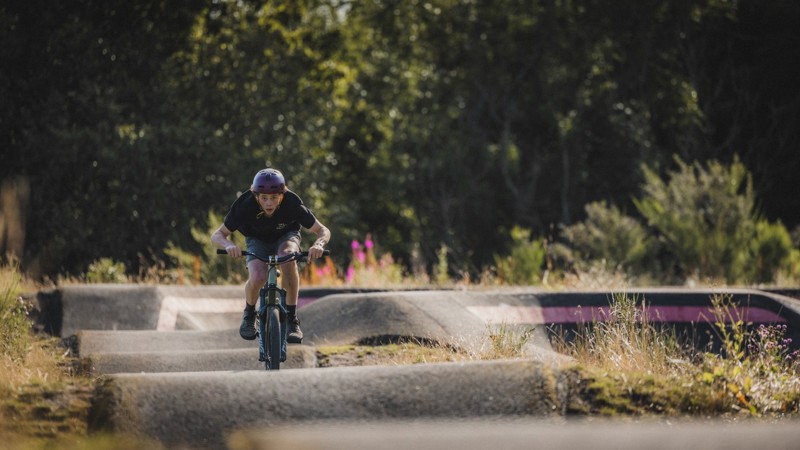 A person on a bike rides along a curving, paved pump track in a park.