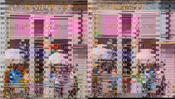 The very pink exterior of Derby Lane cafe with outdoor seating and striped umbrellas.