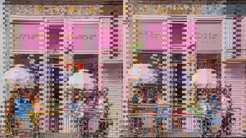 The very pink exterior of Derby Lane cafe with outdoor seating and striped umbrellas.