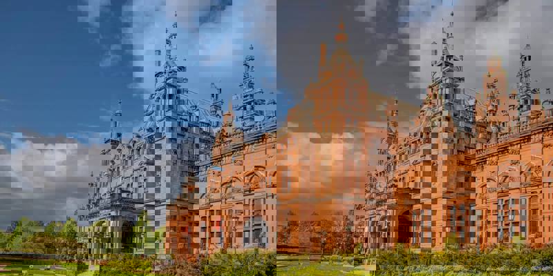A stunning wide shot of the Kelvingrove Art Gallery and Museum, a grand red-brick building with towers and arched entryways, set against a blue sky.