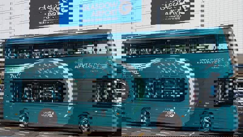 A turquoise First Bus double-decker bus for the Glasgow Airport Express 500 service parked in front of the main terminal building at Glasgow Airport.