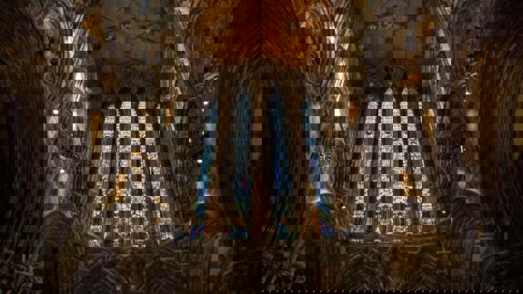 Interior of Glasgow Cathedral with tall stained glass windows and vaulted stone arches.