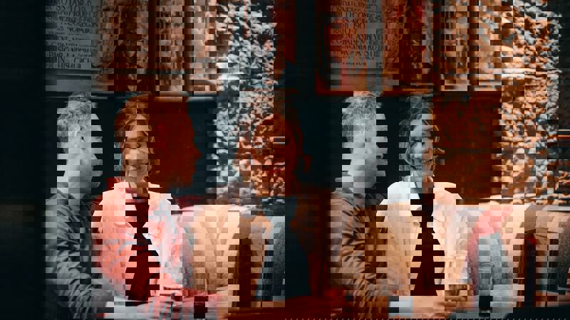 Two people sit close together on a patterned booth in a dimly lit cosy pub. Both are looking contented. In the background, stone walls and framed portraits are visible.