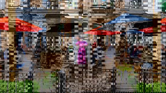Outdoor pub seating with people at wooden tables under red and navy umbrellas.