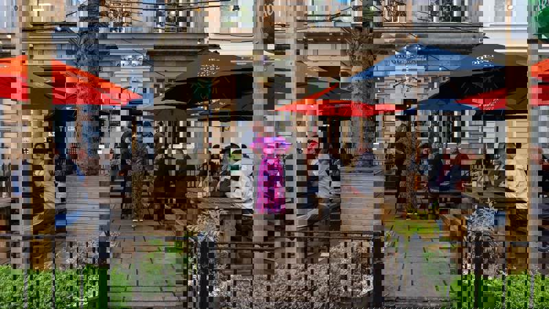 Outdoor pub seating with people at wooden tables under red and navy umbrellas.