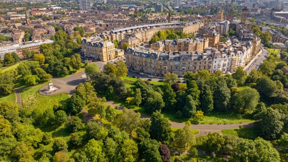 An aerial view of Park Circus within Glasgow's west end. The buildings are surrounded by lots of trees in bloom and the sun is shining.