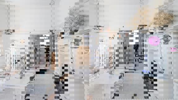 A pristine white room with minimalist furniture, including a table and chairs, and a white fireplace. A stylized floral painting hangs on the wall.