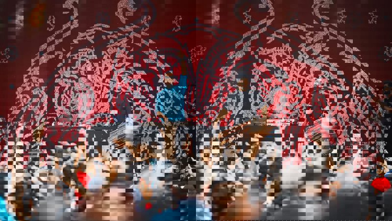 Two men performing on an outdoor stage in front of a large crowd with their arms raised in the air.