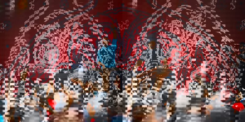 Two men performing on an outdoor stage in front of a large crowd with their arms raised in the air.