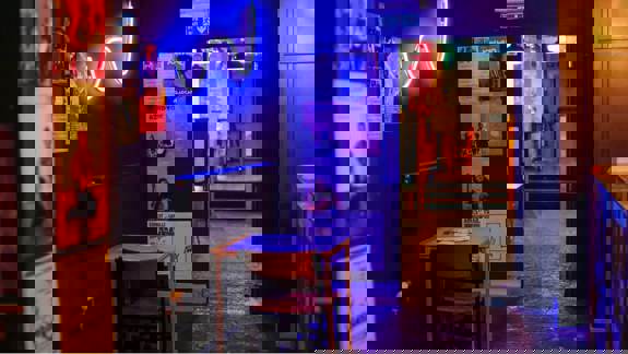 A cozy, dimly lit cafe interior with a small table, a chair, posters on the walls, and a blue neon light.