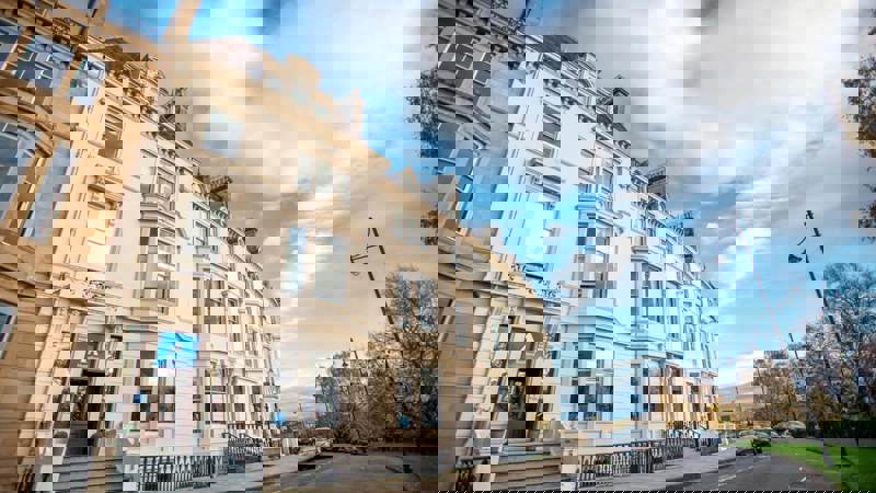  A wide-angle, low-view photo of the Glasgow Youth Hostel, a large, light-coloured Victorian building with bay windows, set against a bright, cloudy sky.