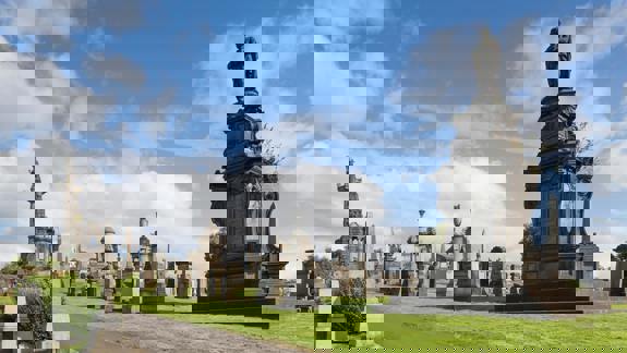 A wide view of the Glasgow Necropolis cemetery on a sunny day, showing multiple large monuments and gravestones.