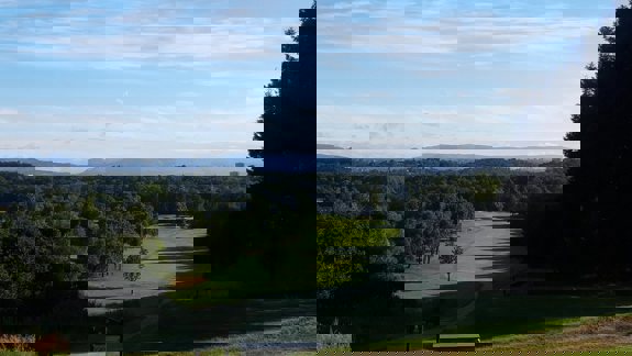 View from a tee at a Glasgow golf course, looking down a tree-lined fairway with rolling hills and the city skyline in the distance.