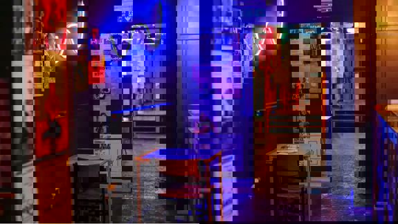 Interior view of the Glad Café, showing posters on the wall, neon signage, and tables in a dimly lit corridor.