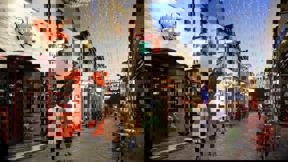 Evening view of Ashton Lane, Glasgow, with Vodka Wodka bar entrance, twinkling overhead lights, and people walking along the cobbled street.