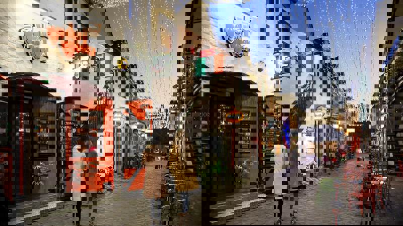 Evening view of Ashton Lane, Glasgow, with Vodka Wodka bar entrance, twinkling overhead lights, and people walking along the cobbled street.