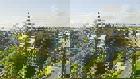 An aerial view of Glasgow Cathedral, a large historic building with a green roof, surrounded by trees and a cemetery, with the wider city in the background.