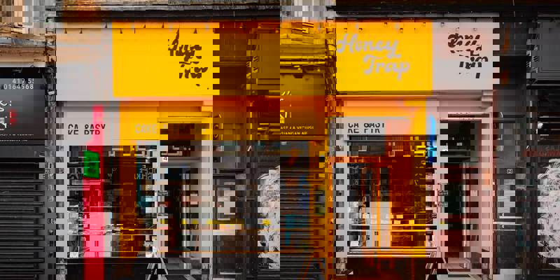 The bright yellow exterior of a shop named Honey Trap, advertising "CAKE & PASTRY" with a front window display.