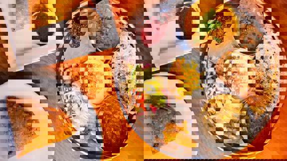 An overhead shot of two plates of Indian food, one with a thali platter and the other with a samosa.