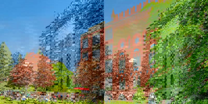 A view of a large, modern building with a grassy lawn and people sitting at tables outside.