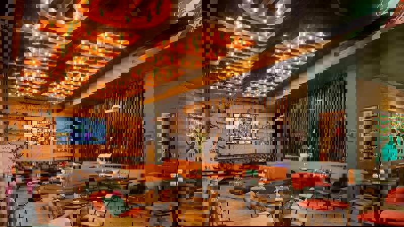 Bar area at Moxy Glasgow SEC featuring bright murals, drum decorations, neon lighting, and casual seating with a lively, playful design.