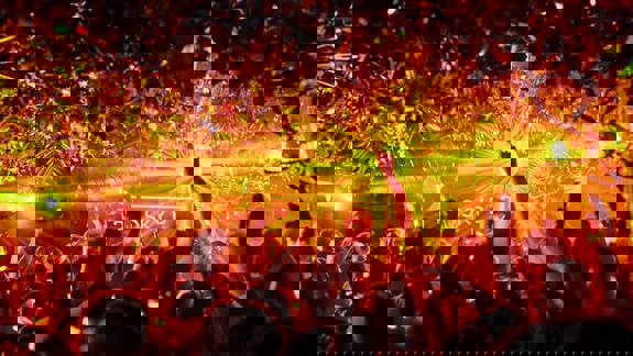 A crowd of people with their hands in the air at a lively music event, with bright lights and a disco ball.