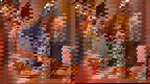 Family seated at a restaurant table, with one adult serving food and another holding a child.