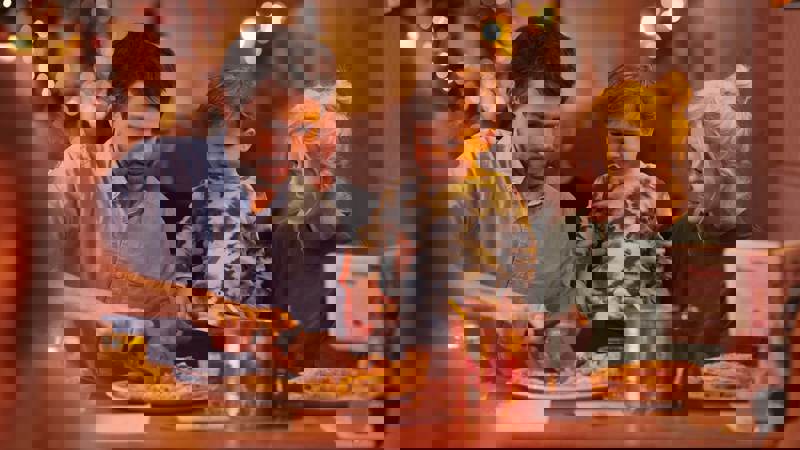 Family seated at a restaurant table, with one adult serving food and another holding a child.