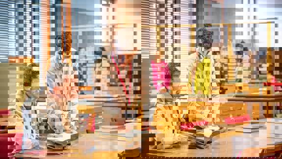 Two men examine a large, old book on a wooden table in a library.