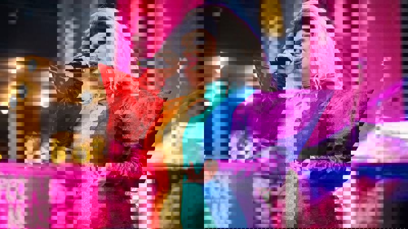 A person in drag with a big white wig and a shimmery rainbow-colored dress is singing into a microphone on a stage.