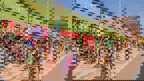 A street view of a market with mannequins and clothing racks outside a row of green and red shops.