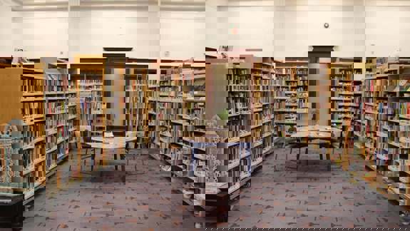 The interior of a library, with bookshelves lining the walls and a round table and chairs in the center.