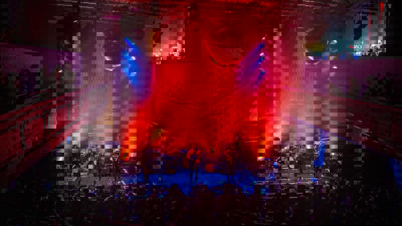Live band plays on a stage bathed in red light under a large disco ball in the Saint Luke's Glasgow music venue.