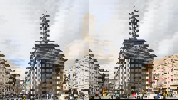 The classical facade of a museum with a statue of a man on a horse in front.